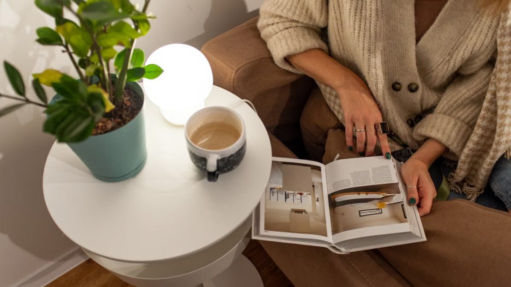 A warm, inviting scene of a person reading and enjoying coffee in an indoor setting with a plant beside them.